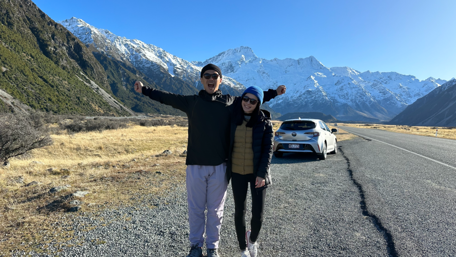 A couple happily posing with a GO Rentals vehicle and mountain landscape in the background.