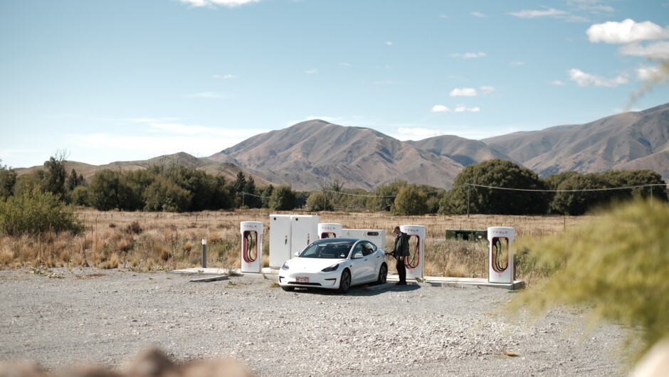 A person charging their GO Rentals Tesla vehicle at a Tesla charging station in South Island with mountain surroundings.