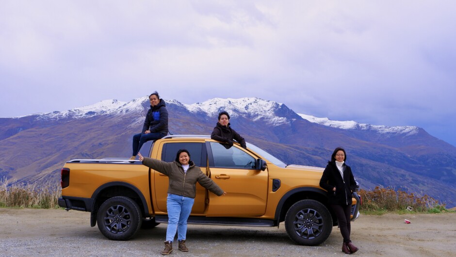 A group of friends posing outside a GO Rentals Toyota Wildtrak vehicle with Queenstown mountain background.