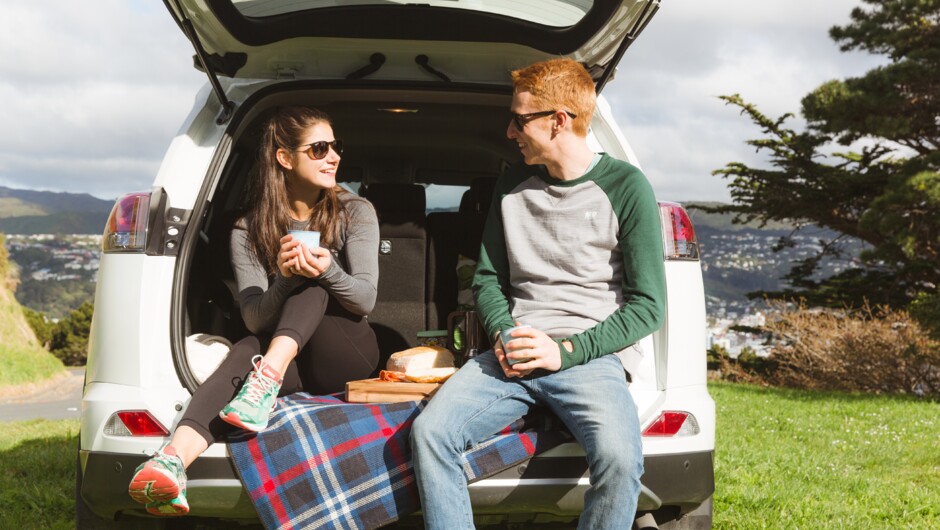 A couple having a picnic sitting in the boot of a GO Rentals vehicle.