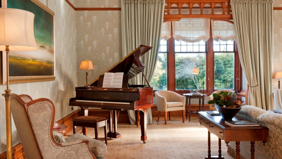 The Drawing Room at Otahuna Lodge features elegant wallpaper, original stained glass and a vintage Edwardian piano.