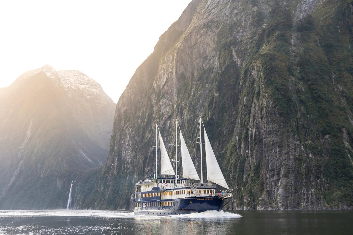 Magnificent Milford Sound fjord showcases towering granite cliffs, cascading waterfalls, and pristine dark waters with cruise ship sailing through.