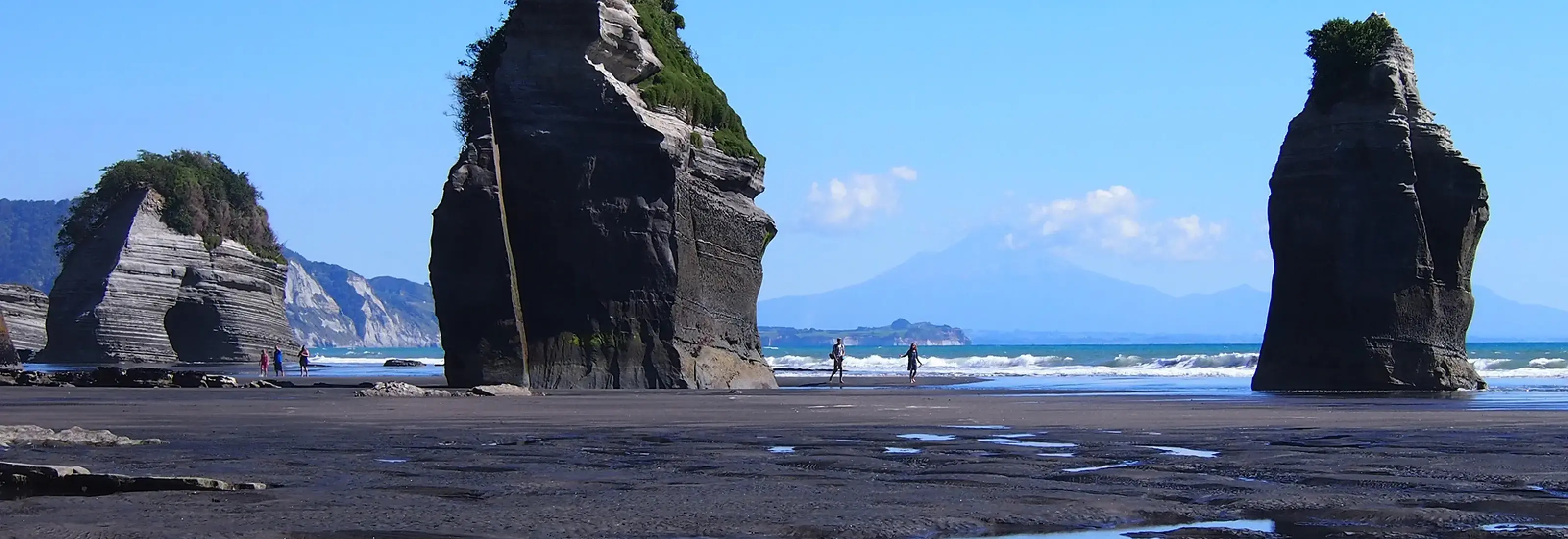 Dramatic Three Sisters rock formations rise from black volcanic sand beach at low tide. 