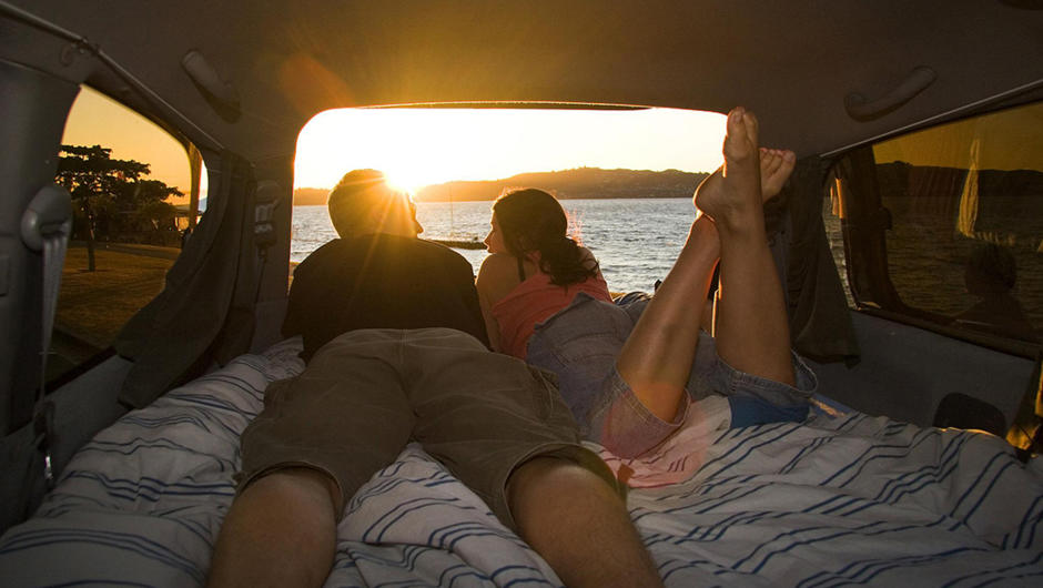 Couple watching the sun set from their Spaceships camper as another day comes to an end in paradise.