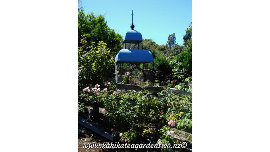 The bird aviary at Kahikatea Gardens enjoys a sunny spot next to climbing roses.