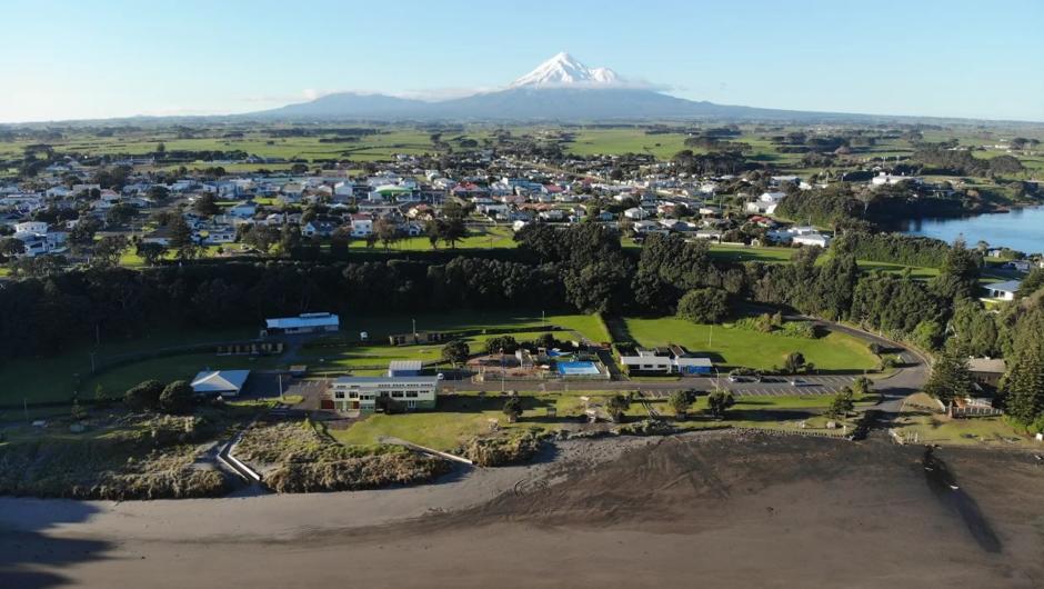 Aerial shot looking back at Opunake Beach and the Opunake Beach Holiday Park with Opunake Lake and the majestic Mt Taranaki in the background.