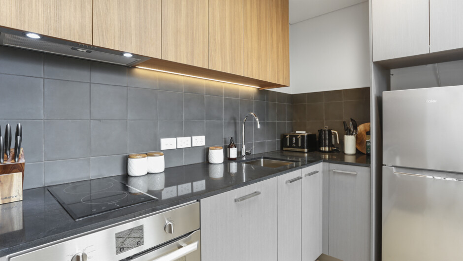 Modern styled kitchen comes with cooking essentials such as a microwave, fridge, oven, dishwasher, and a cooktop.