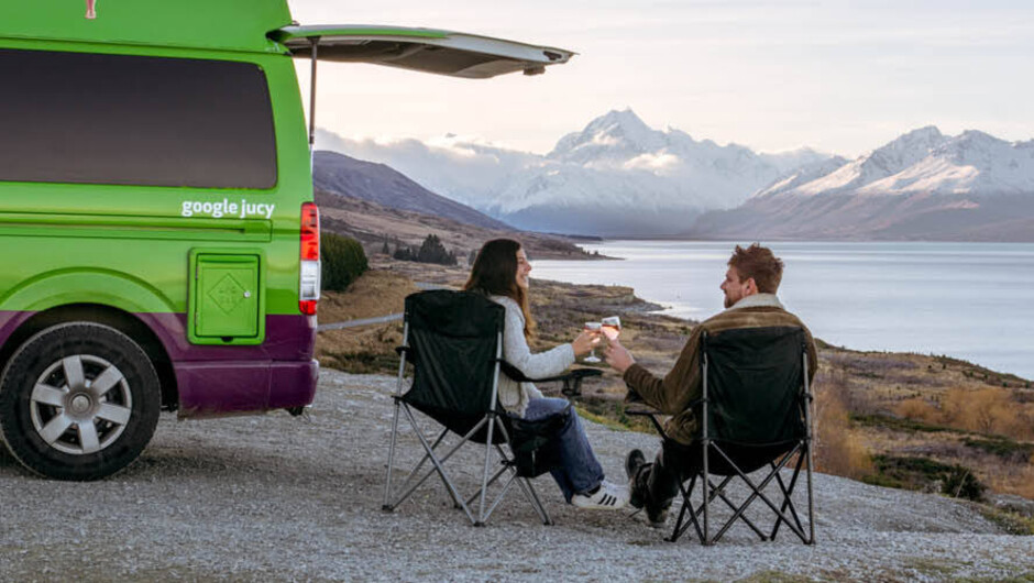 Couple sitting  next to JUCY chaser, near Lake Pukaki