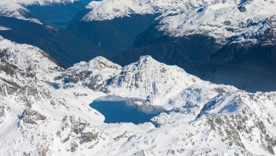 Just one example of a mountain lake surrounded by snow (in winter) during flights to Milford Sound.
