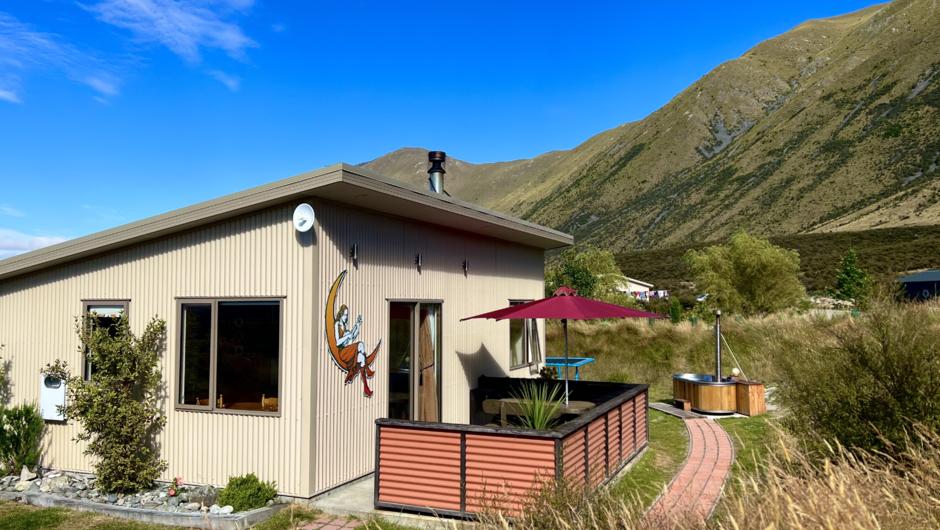 The cosy cottage and wood-fired hot tub during the day, with views of the Ben Ohau mountain range