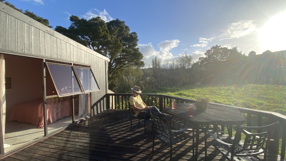 A large deck to the North West with outdoor dining table looks out over a wild field and the Waima River.