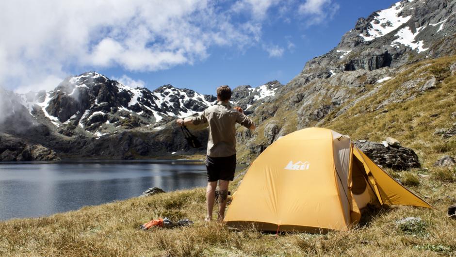 Individual standing by his tent enjoying the views on the side of a mountain lake in Mount Aspiring National Park.