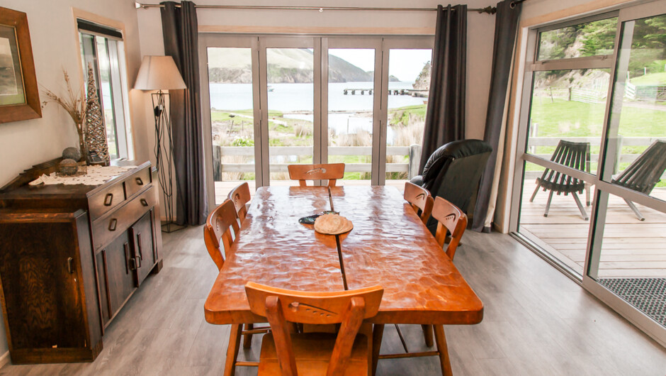 From inside Little Colonsay Beach House, the outlook to the beach is where you can view your boat on the mooring or see activities going on in the Bay. The wooden kauri table is suitable for large groups.
