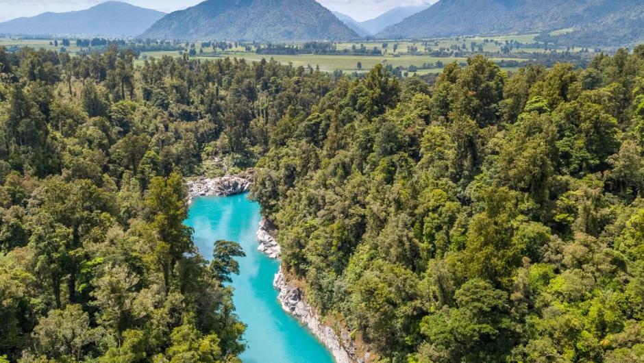 Blue waters flowing through Hokitika Gorge with mountains in the background