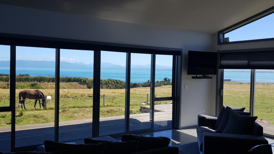 The shared lounge offers more stunning views across the bay. A wood fire offers ambience and warmth, there are two sofas and an open kitchen, bar and dining area where we entertain and cater for our guests.