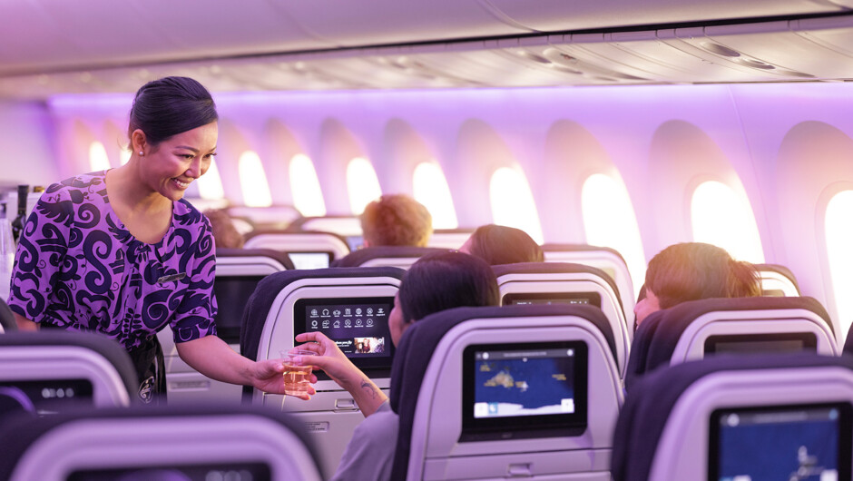 Flight attendant serving drink to passenger in economy