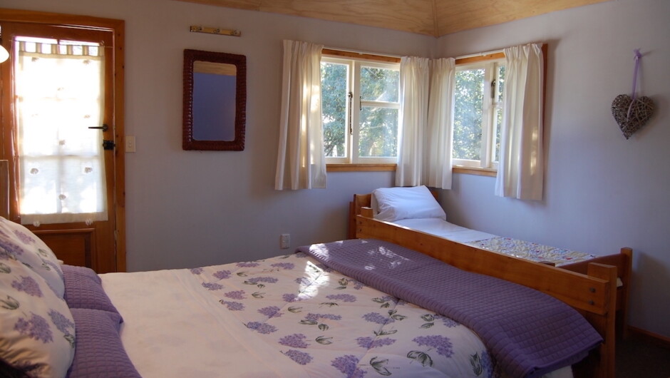 Kowhai bedroom showing both queen and single beds and door to the balcony.