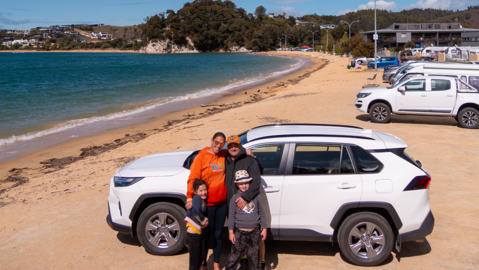 A family posing in front of a GO Rentals vehicle parked alongside Nelson beach.