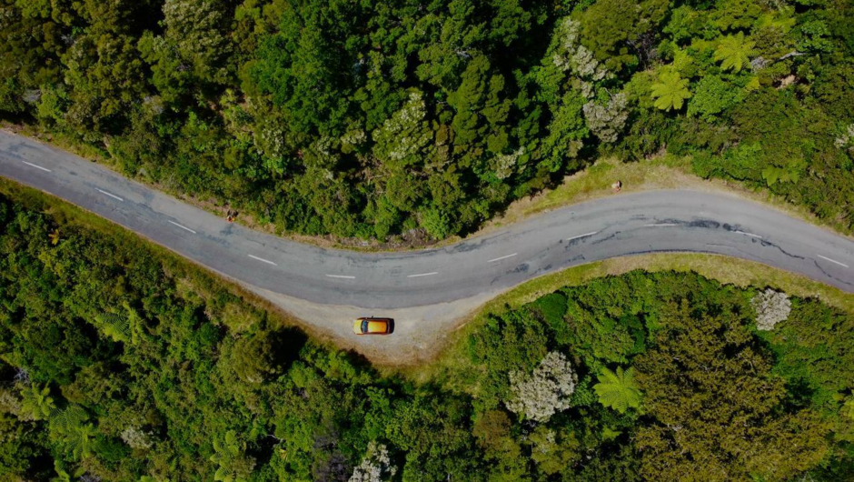Aerial shot of GO Rentals vehicle driving along New Zealand road surrounded by forest landscapes.