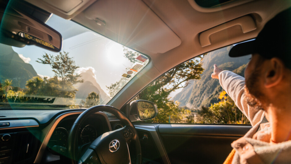 Male person sitting in a GO Rentals car looking out the window pointing at the mountain landscape.