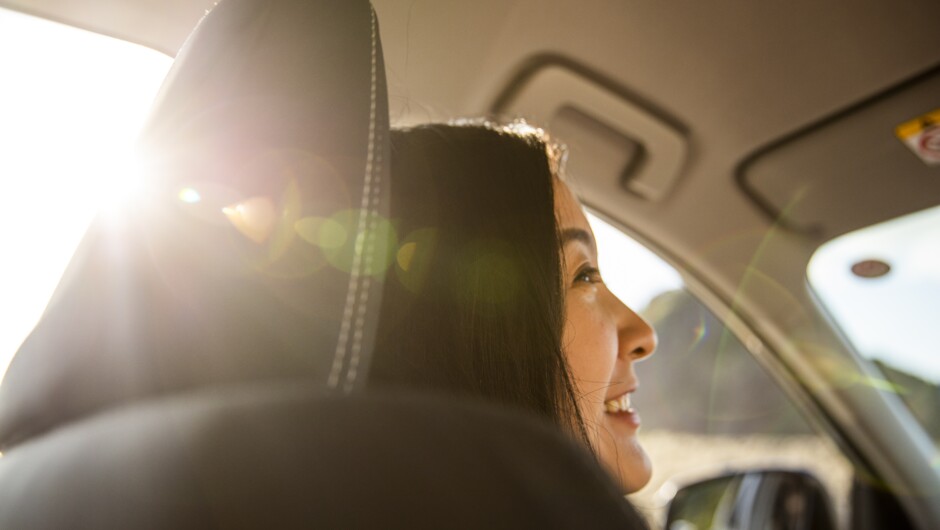 Women smiling sitting in front passenger seat with sun shining through window.