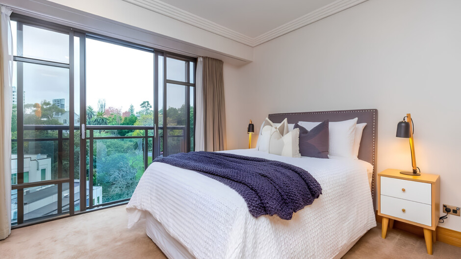 Plush bed next to large windows overlooking the neighbourhood