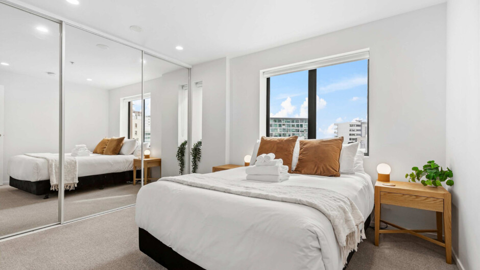 Bedroom with fresh linens and a built-in wardrobe for storage. Large windows provide natural light.