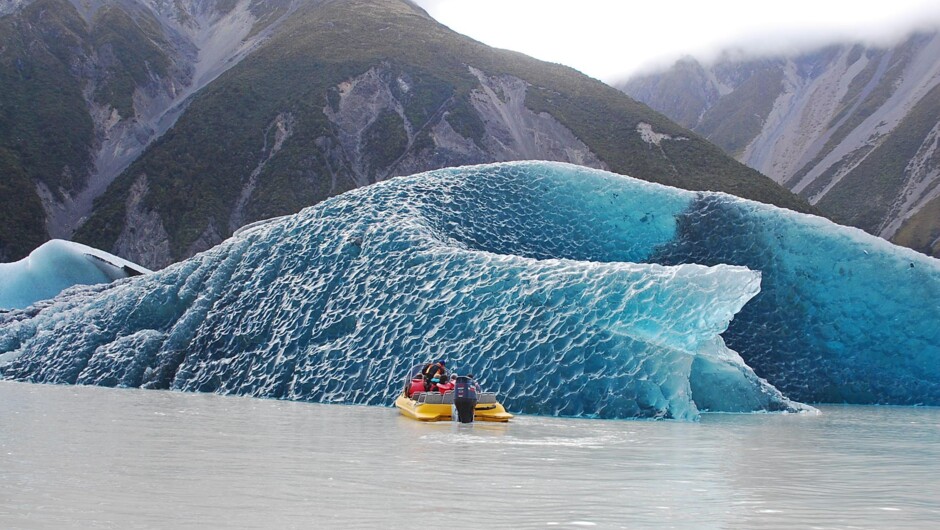 グレイシャー・エクスプローラーズのボートが氷河から崩れ落ちたばかりの青い氷塊に近づきます。